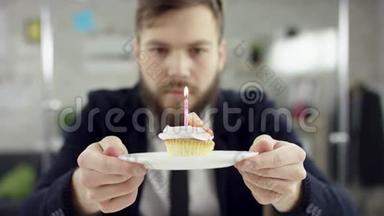 悲伤的商人在办公室里庆祝一个孤独的生日，他一个<strong>小</strong>蛋糕上吹蜡烛。 <strong>小</strong>蛋糕，蛋糕